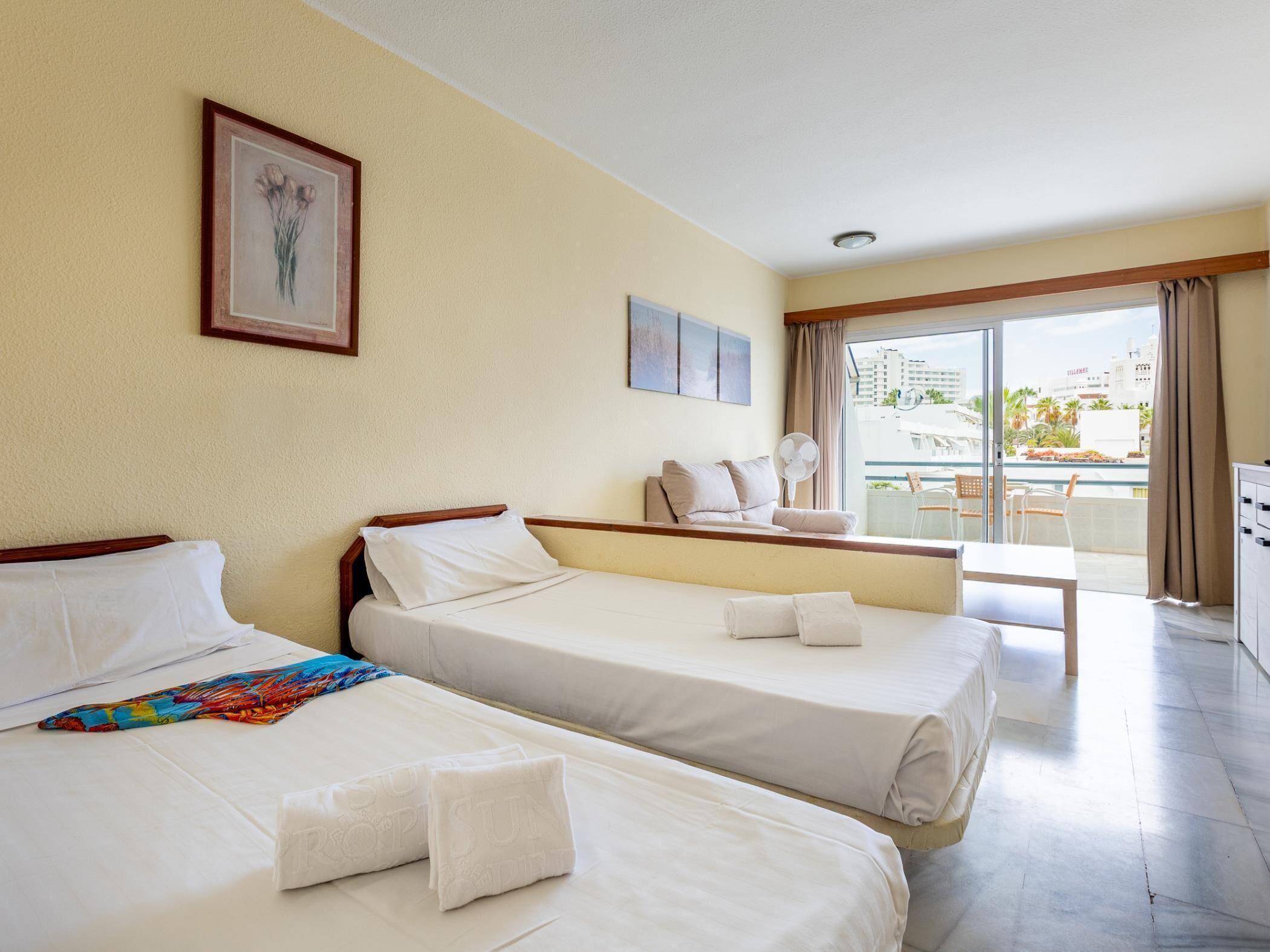 A hotel room with two beds, a balcony, and a city view.