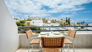 Un balcón con una mesa preparada para dos personas, con vista a una ciudad costera con palmeras y edificios.