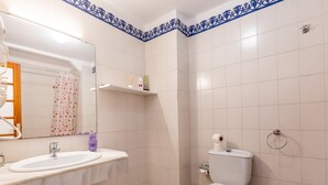 Un baño con lavamanos blanco, inodoro y bidé. Hay un espejo sobre el lavamanos y una repisa con artículos de tocador.