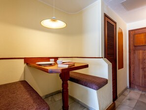 Habitación de esquina con un banco de madera, una mesa con un plato blanco, una taza y un libro.