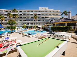 A pool area with lounge chairs, a pool table, and a building with multiple balconies in the background.