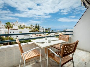 A balcony with a table and chairs, overlooking a coastal cityscape with buildings and palm trees.