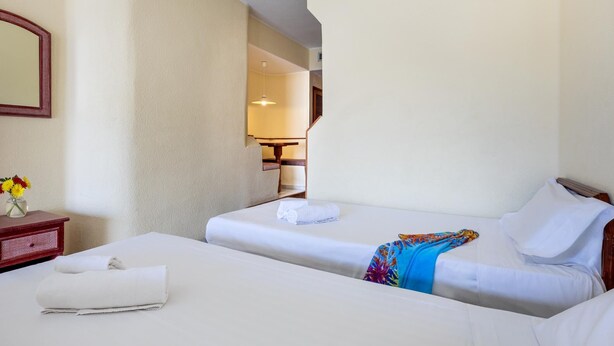 A hotel room with two beds, a bedside table with a vase of flowers, and a mirror on the wall. - Lovely Studio Club Atlantis (Costa Adeje)