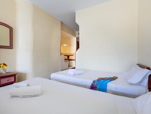 Habitación de hotel con dos camas, una mesita de noche con un florero y un espejo en la pared.