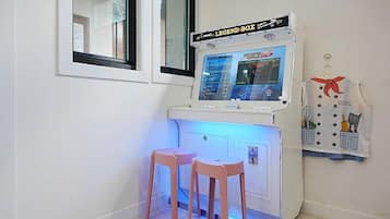 A gaming station with a screen, two pink stools, and a wall-mounted towel rack with a towel.