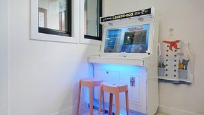 En spillestation med skærm, to lyserøde taburetter og et vægmonteret håndklædetørrestativ med håndklæde.
