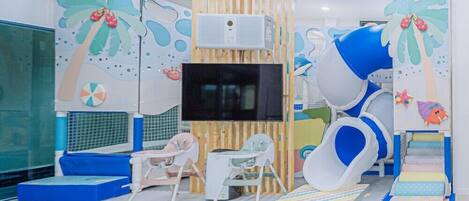 Un'area giochi per bambini con uno scivolo, tappetini e un televisore montato a parete.