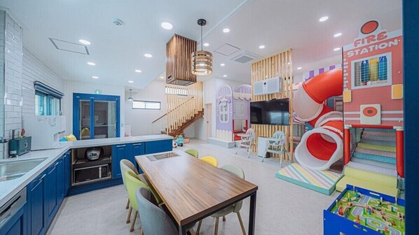 A modern kitchen with blue cabinets, a wooden dining table, and a children's play area with a slide. - My Kids Pool Villa (Taean)
