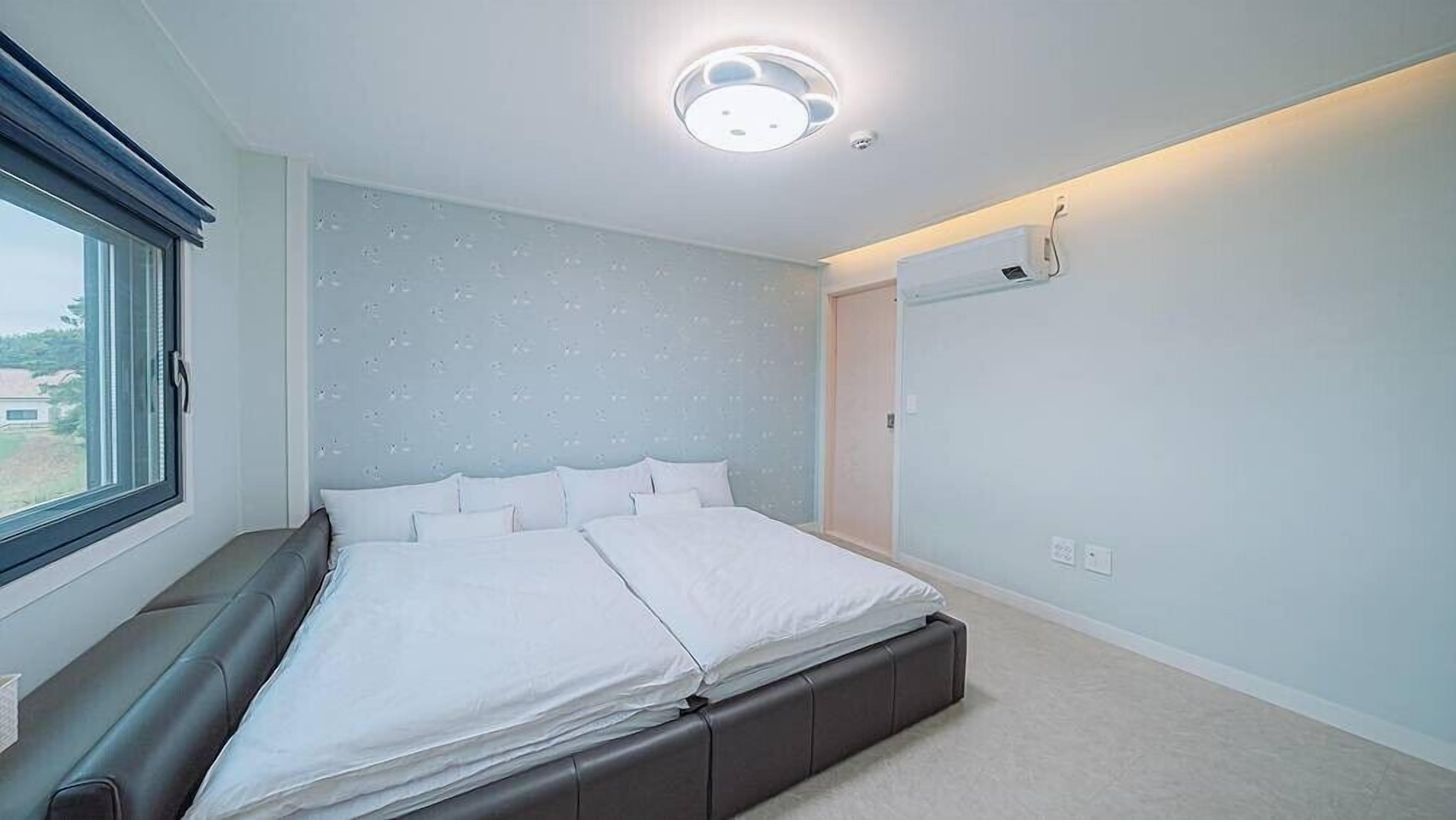 Ein modernes Schlafzimmer mit Bett, Fenster und Deckenleuchte.