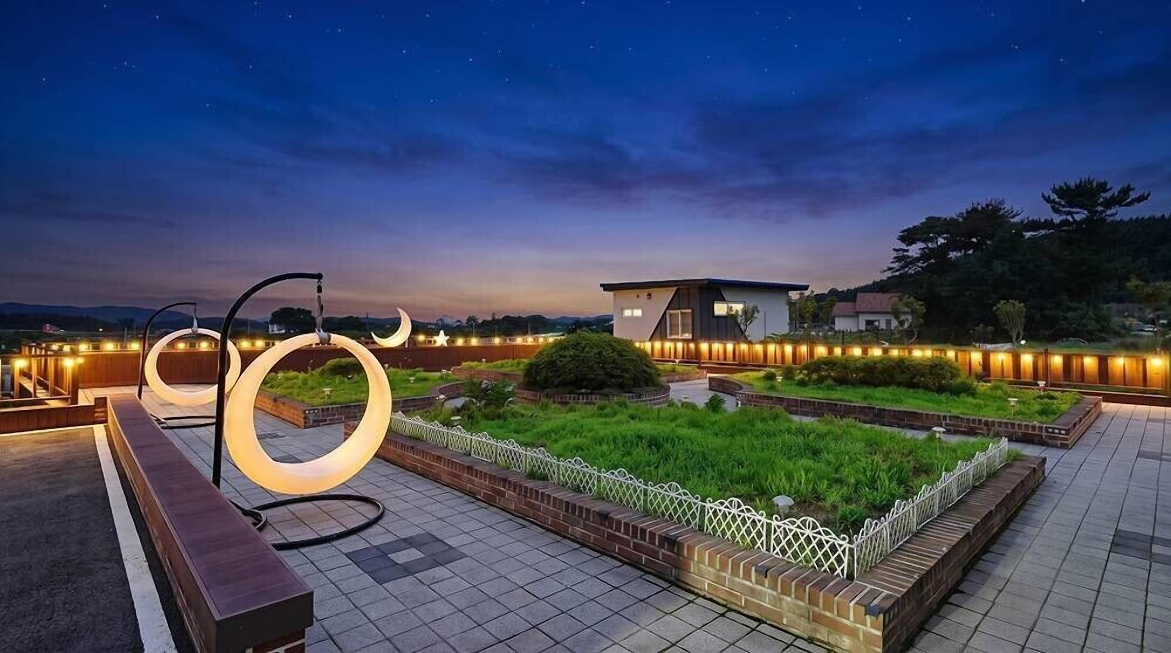 A rooftop garden with circular light fixtures, a white fence, and a building in the background.
