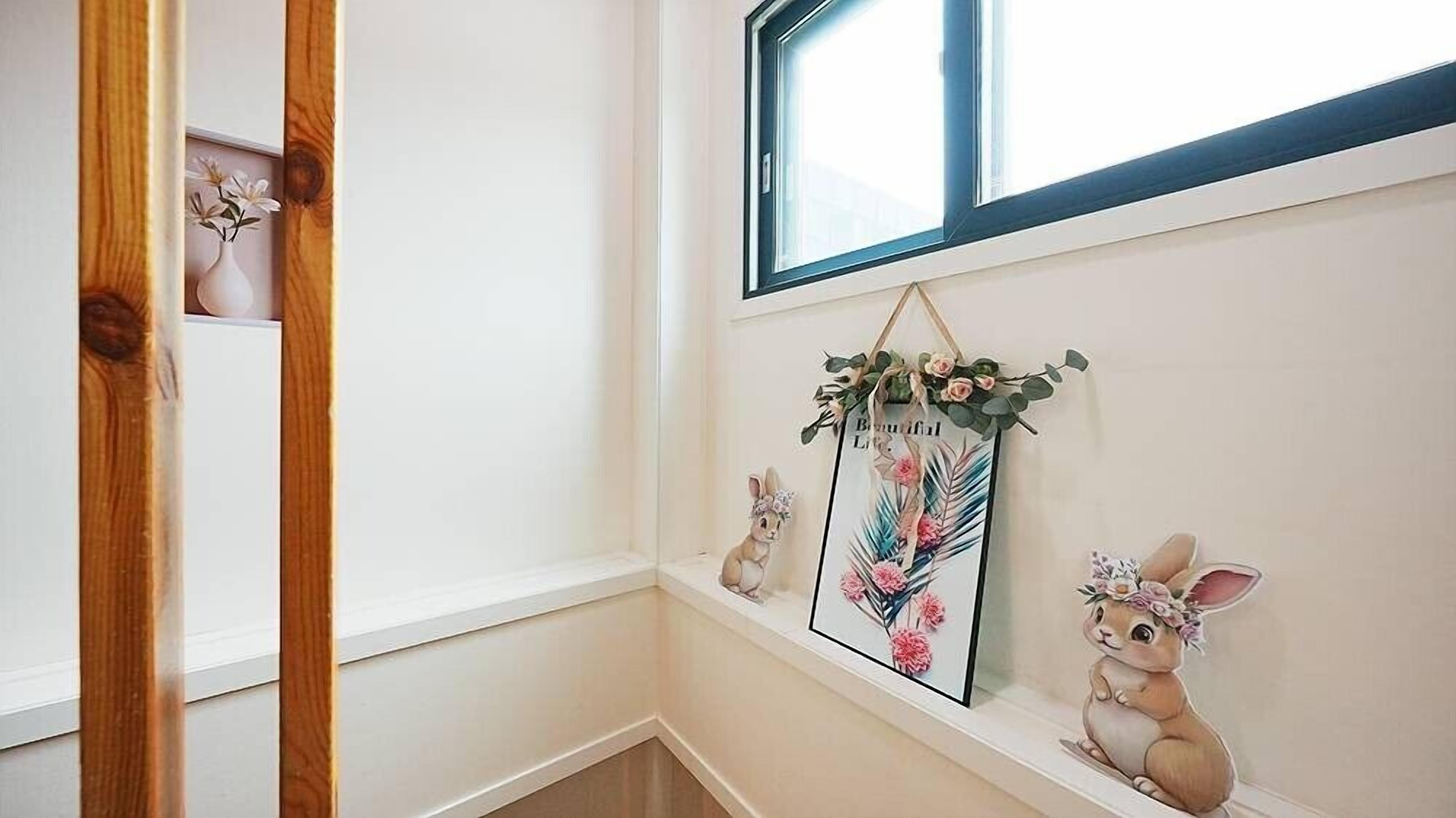 Un pasillo con una puerta de madera, un ventanal y adornos en la pared, incluyendo un cuadro enmarcado y dos figuritas de conejos.
