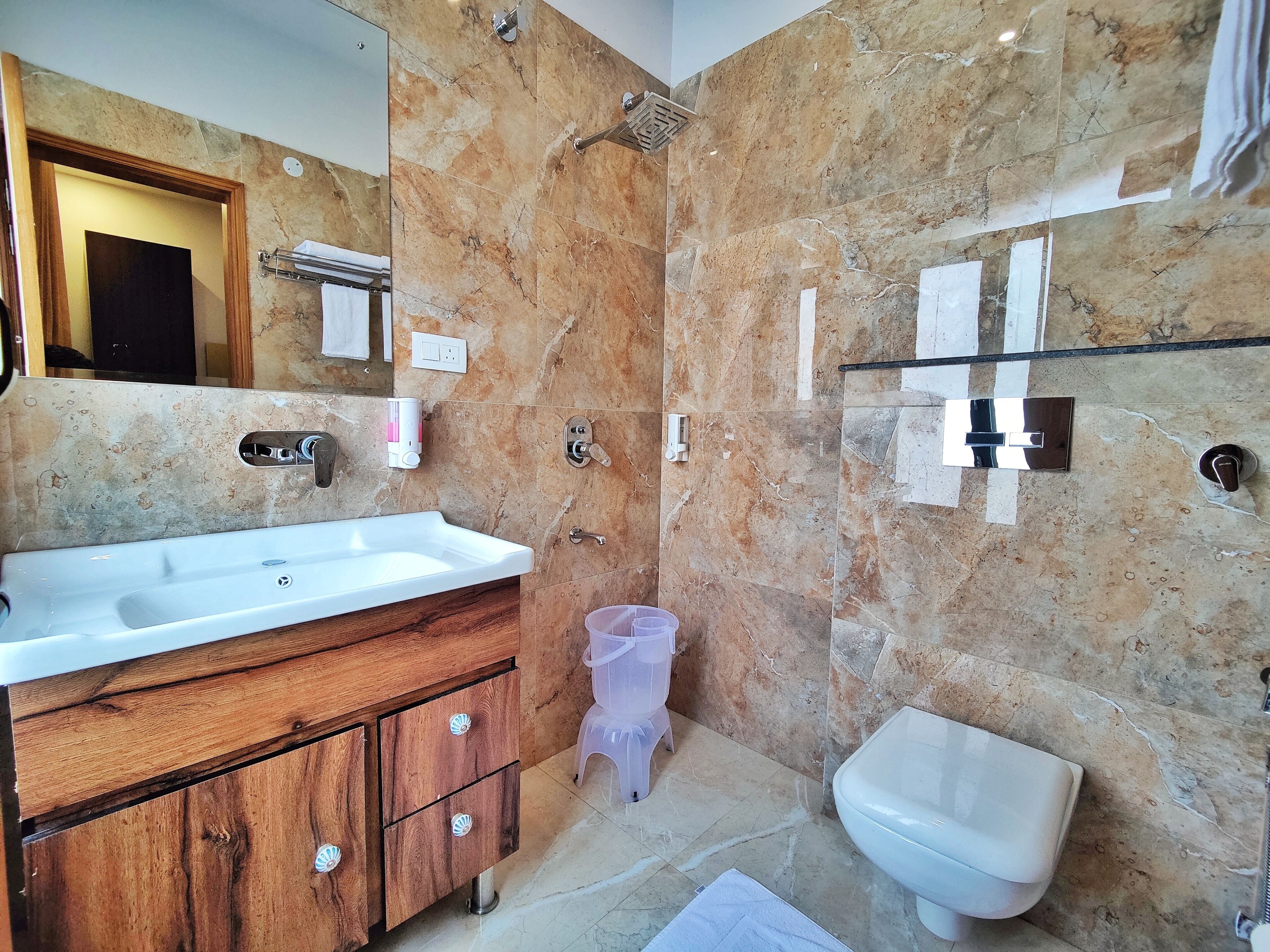 A bathroom with a marble wall, a wooden vanity, a white sink, a glass shower enclosure, and a white toilet.