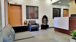 A reception area with a reception desk, a blue armchair, a sofa, and a decorative statue. - Hotel Park Hills (Mohali)