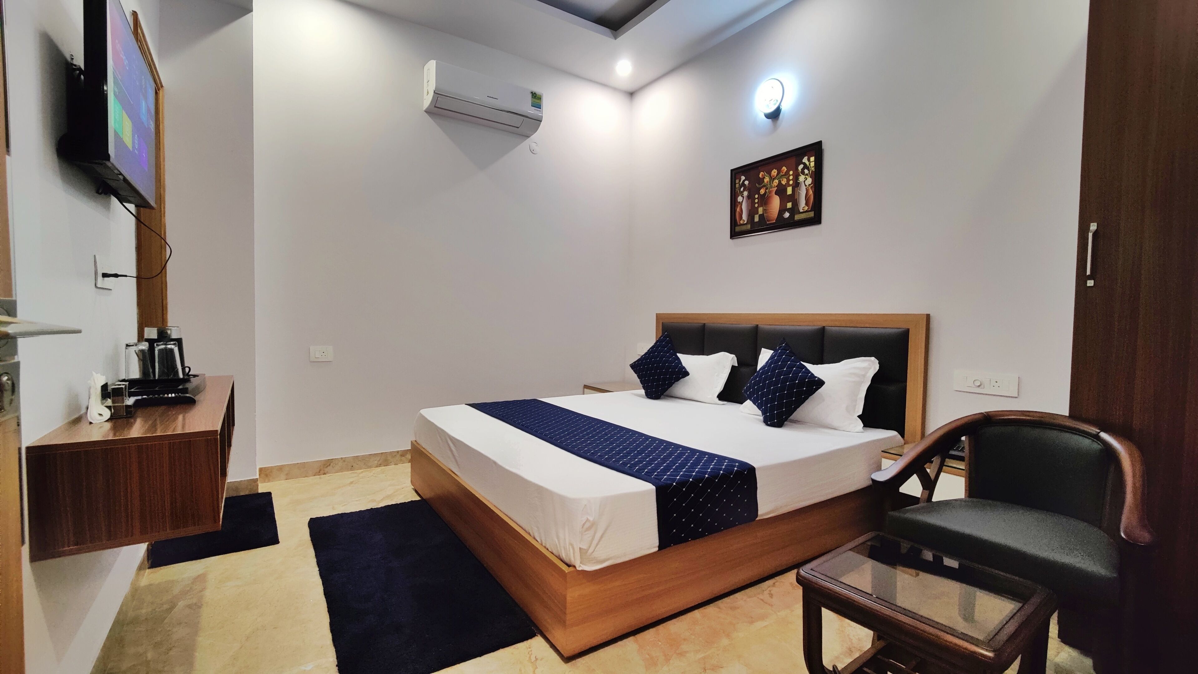 A hotel room with a bed, bedside table, chair, and a flat-screen TV mounted on the wall.