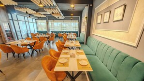 A restaurant with a long table set for a meal, orange chairs, and a green booth. - Hotel Park Hills (Mohali)