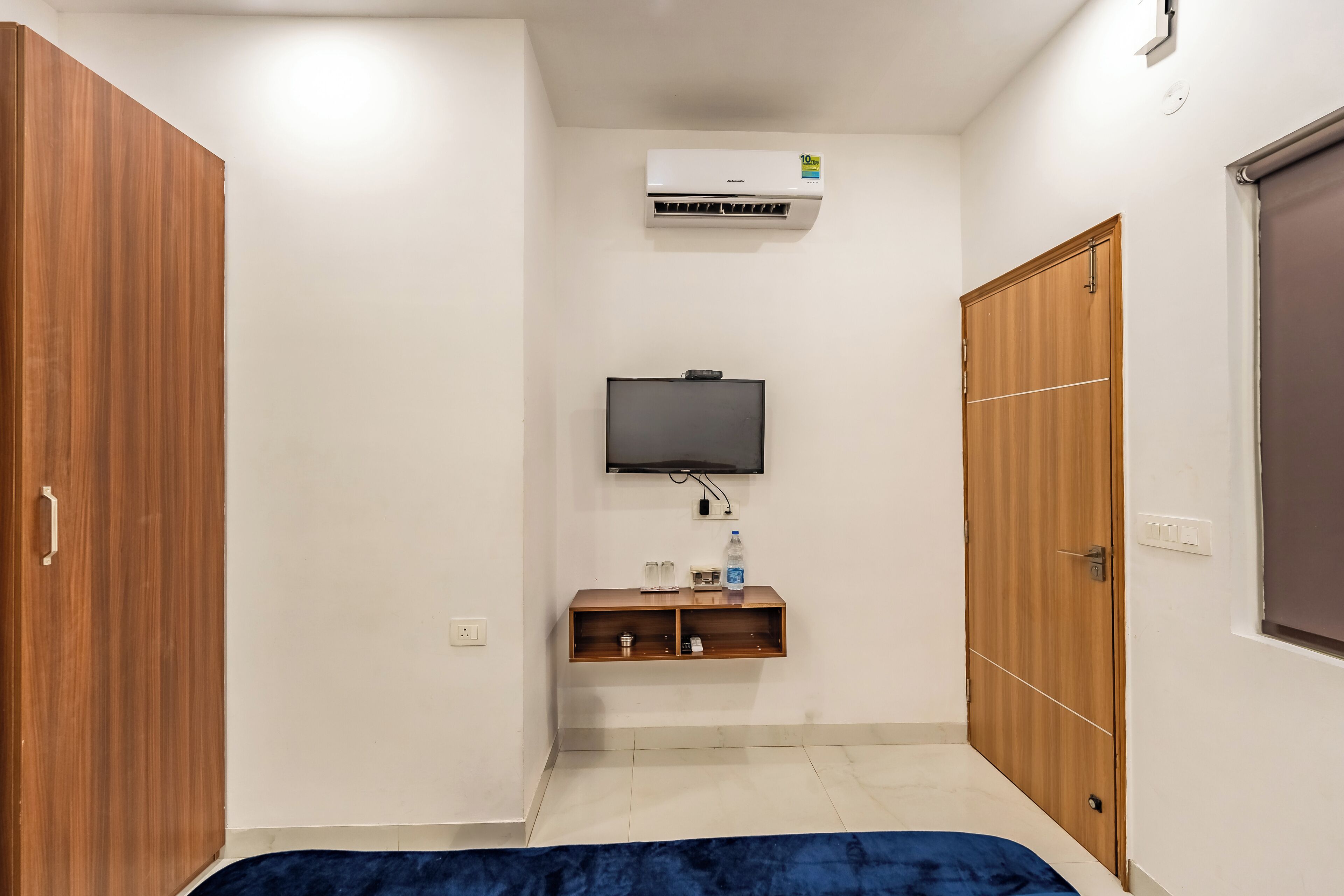 A bedroom with a bed, wardrobe, TV, air conditioning unit, and a small shelf with items.