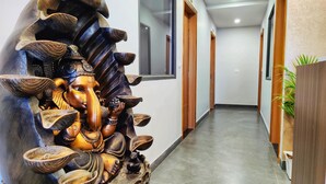 A hallway with a large wooden statue of a deity, wooden doors, and a potted plant. - Hotel Park Hills (Mohali)
