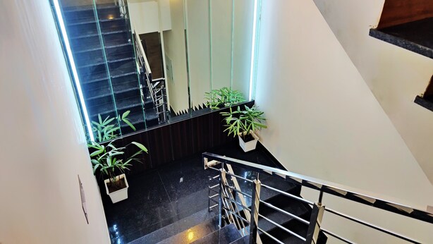A modern staircase with glass railings, potted plants, and a polished floor. - Hotel Park Hills (Mohali)