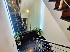 En moderne trappe med glasgelændere, krukker med planter og en poleret gulv.