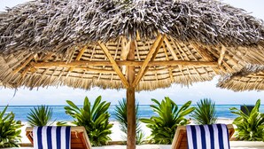 Two wooden lounge chairs with blue and white striped towels, a thatched umbrella, and a view of the ocean. - Alladin Beach Hotel and SPA Zanzibar (Matemwe)