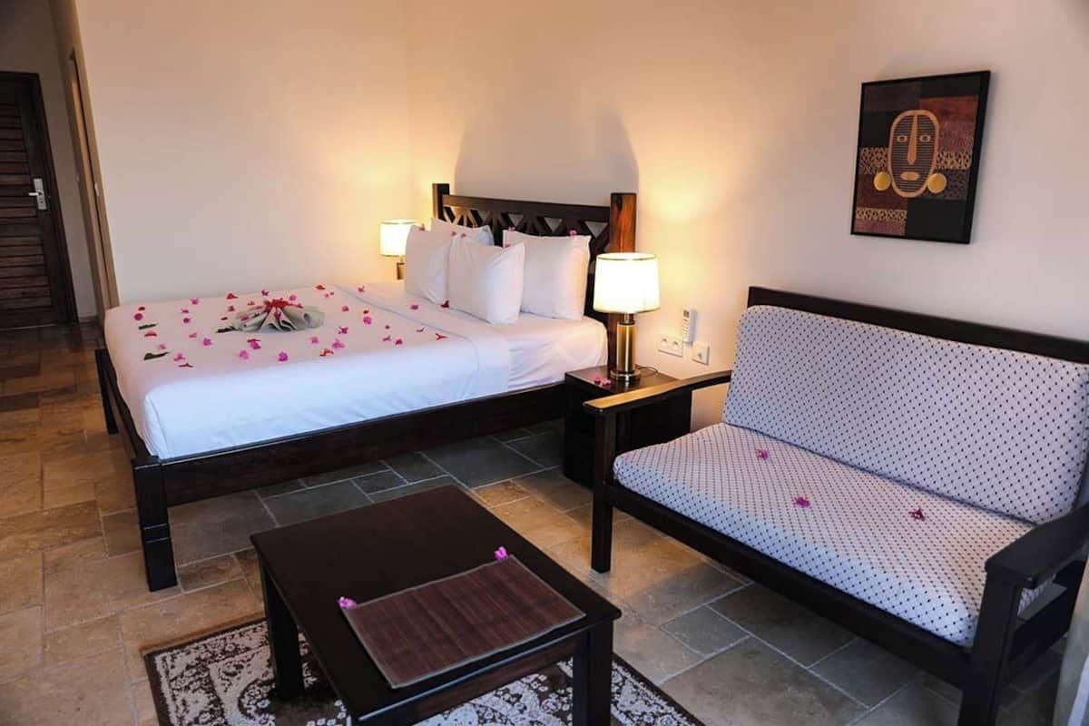 A hotel room with a bed, a sofa, a nightstand, and a wall-mounted artwork.