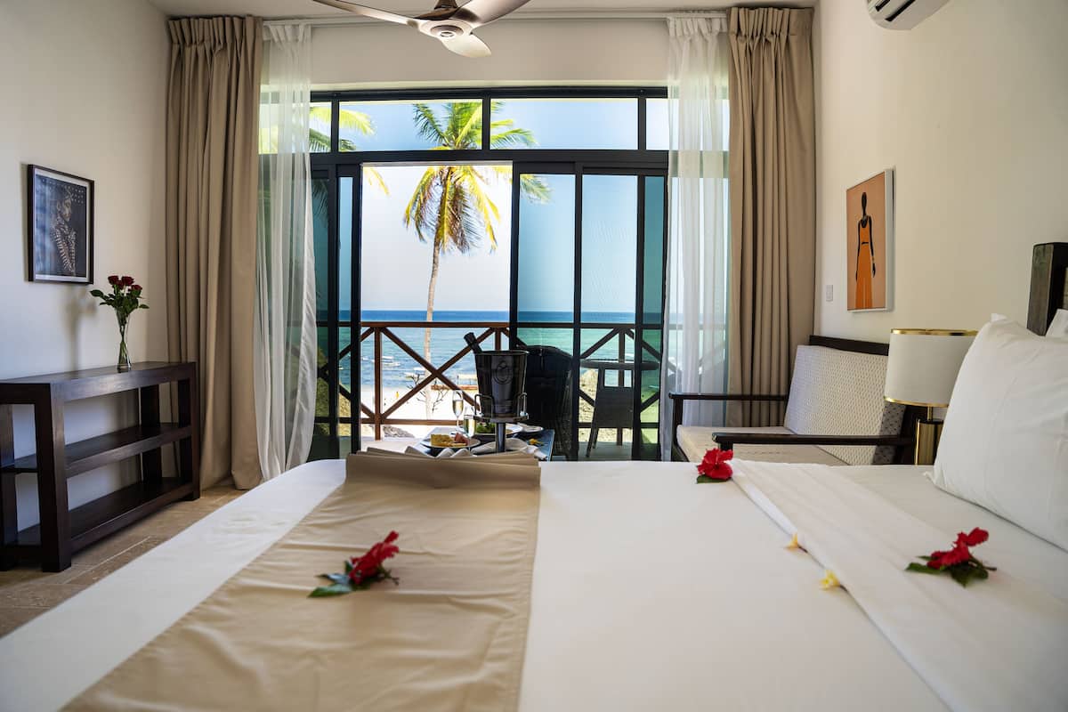 A hotel room with a large bed, a desk, a chair, and a view of the beach.