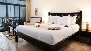 A hotel room with a large bed, a nightstand, a bedside table, a window with curtains, and a view of the outdoors. - Alladin Beach Hotel and SPA Zanzibar (Matemwe)