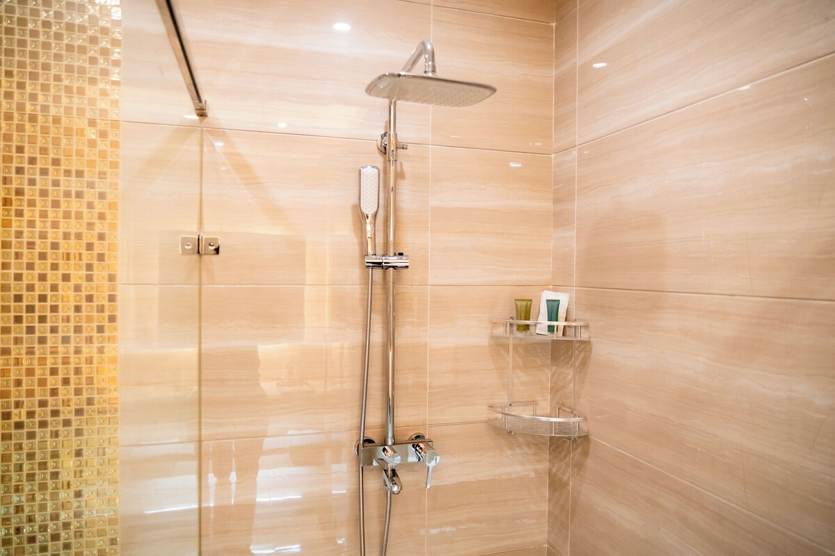 Une salle de bain moderne dotée d’une douche à parois de verre, d’un pommeau de douche à main et d’un robinet mural.