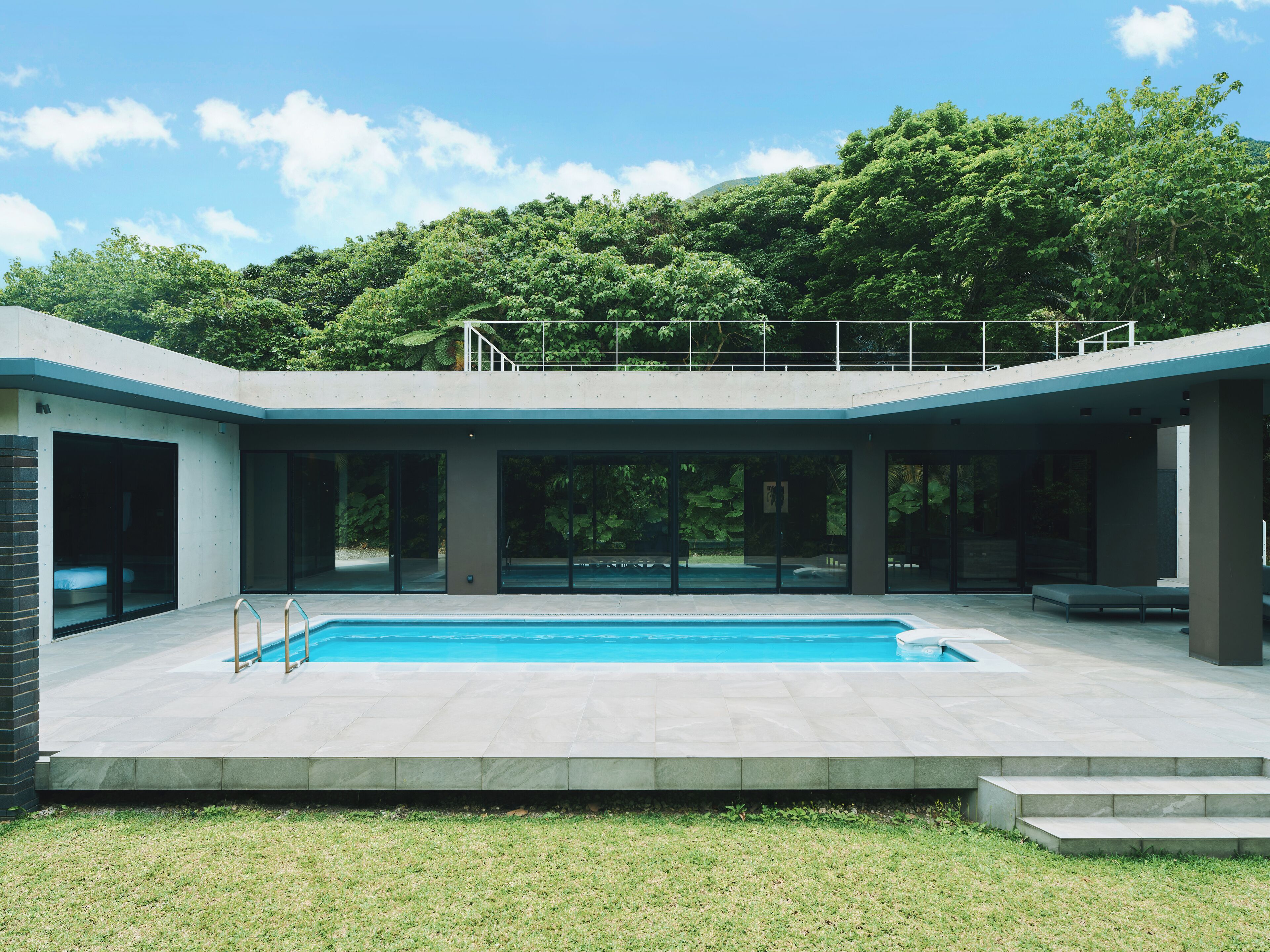 Una casa moderna amb piscina, portes de vidre grans i un balcó amb vista a una zona verda i exuberància.