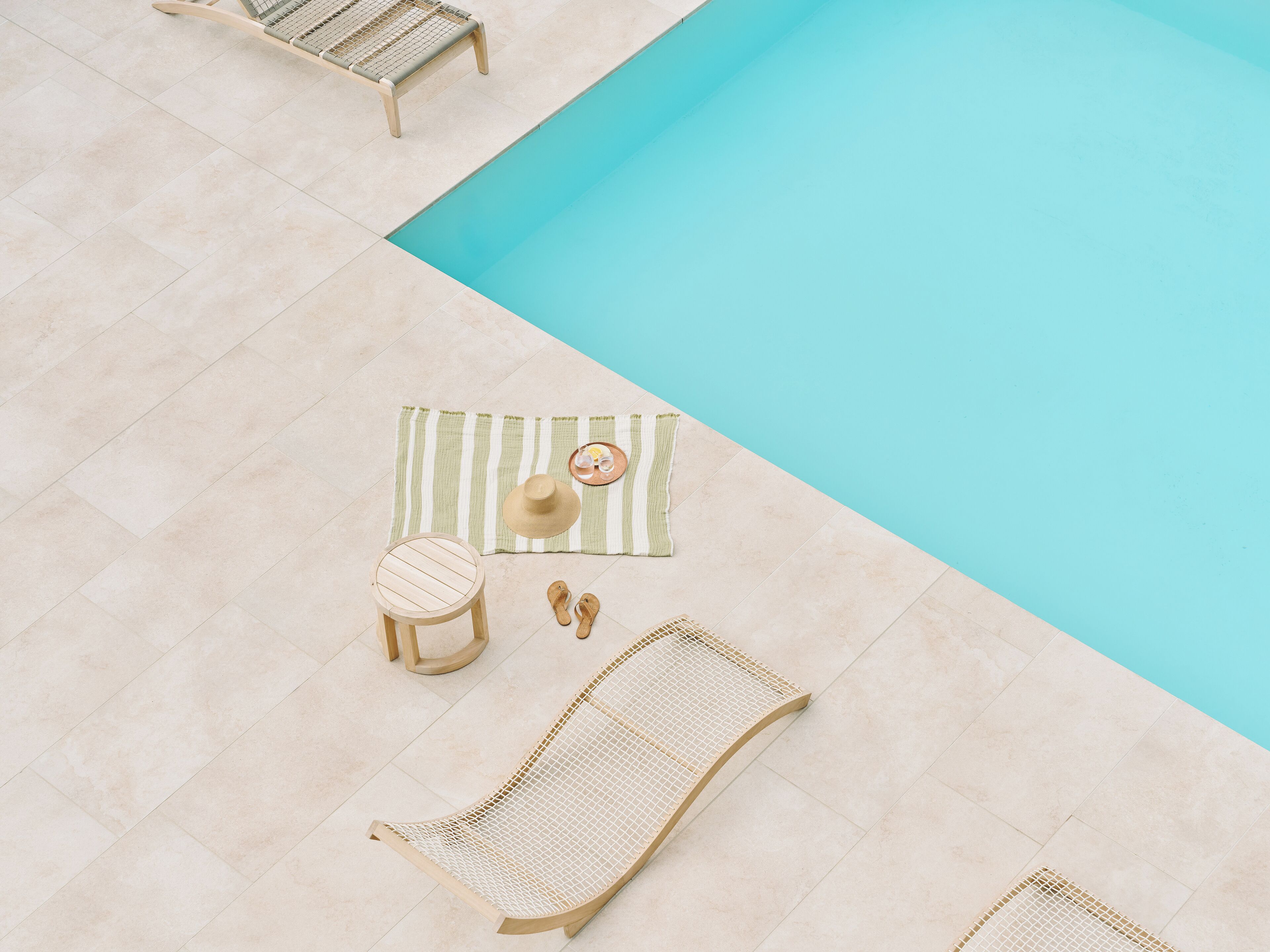 A poolside area with a lounge chair, a small stool, a hammock, and a striped mat.