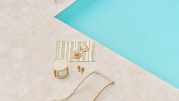 A poolside area with a lounge chair, a small stool, a hammock, and a striped mat.