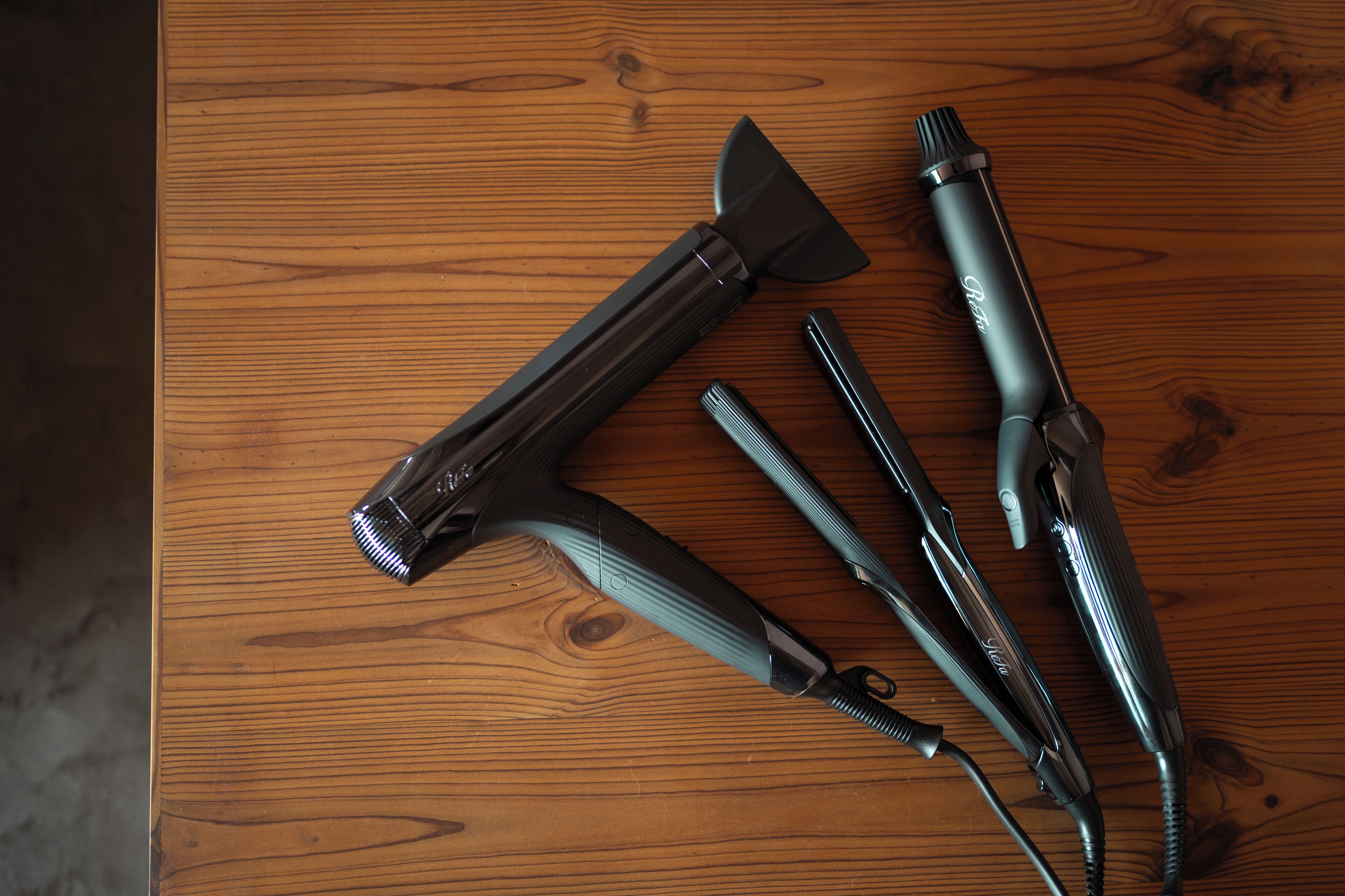 A wooden table with four hair styling tools laid out.
