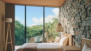 A bedroom with a large bed, a stone wall, a view of greenery, and a hanging light fixture. - Villa El Cielo Ishigaki (Ishigaki)
