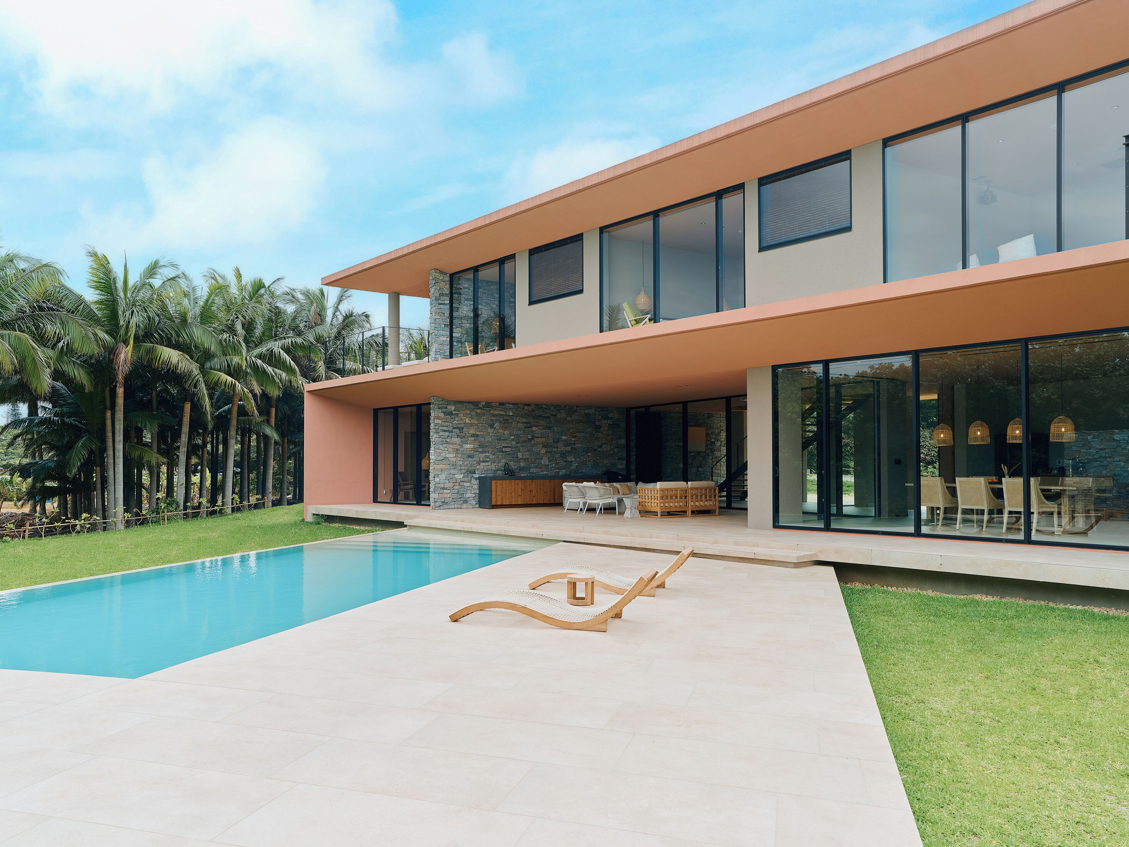 Una casa moderna de dos pisos con piscina, mobiliario exterior y un muro de piedra.