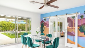 Un espace repas moderne avec une table en verre, des chaises de couleur turquoise et une vue sur un jardin aménagé.