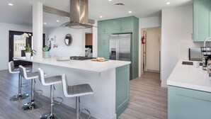 Une cuisine moderne dotée d’un îlot central, de tabourets de bar, d’un réfrigérateur en acier inoxydable et de meubles de couleur turquoise.