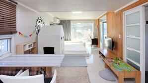 Ein modernes Hotelzimmer mit Bett, Fernseher, einer kleinen Spielecke und einem Fenster mit Jalousien.
