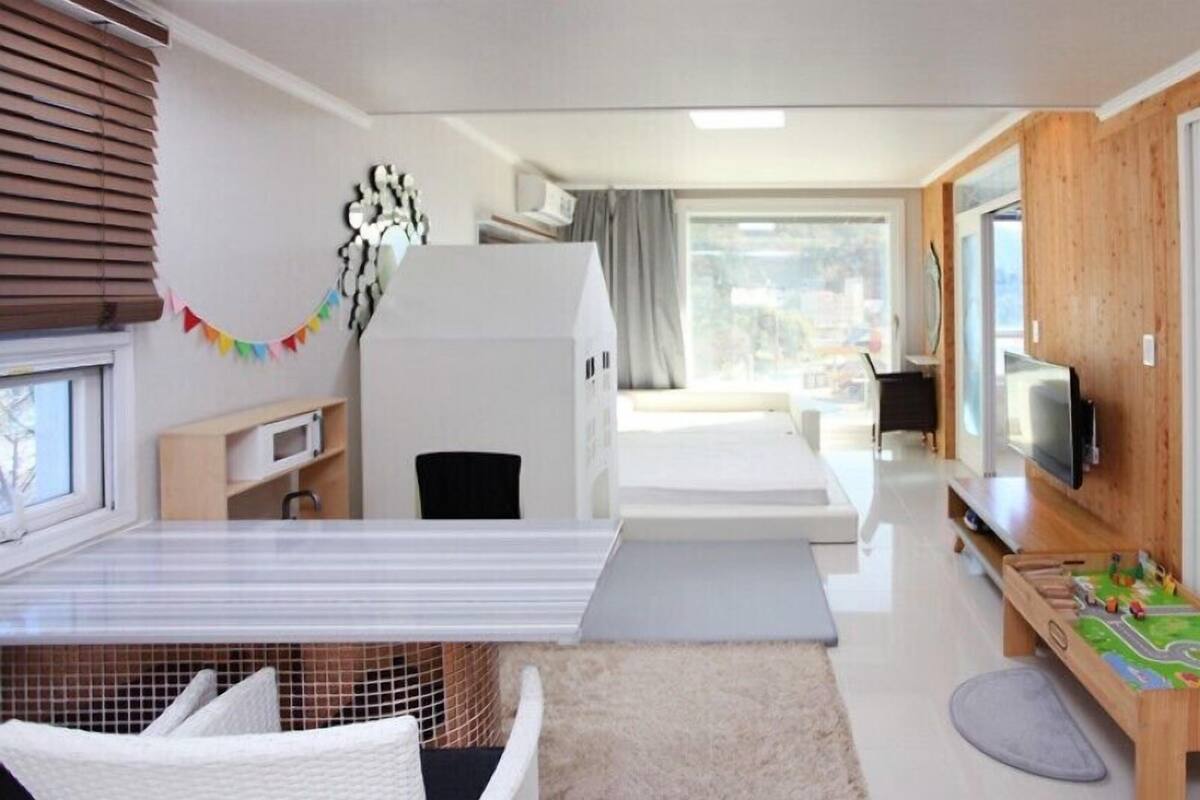 A modern hotel room with a bed, a TV, a small play area, and a window with blinds.
