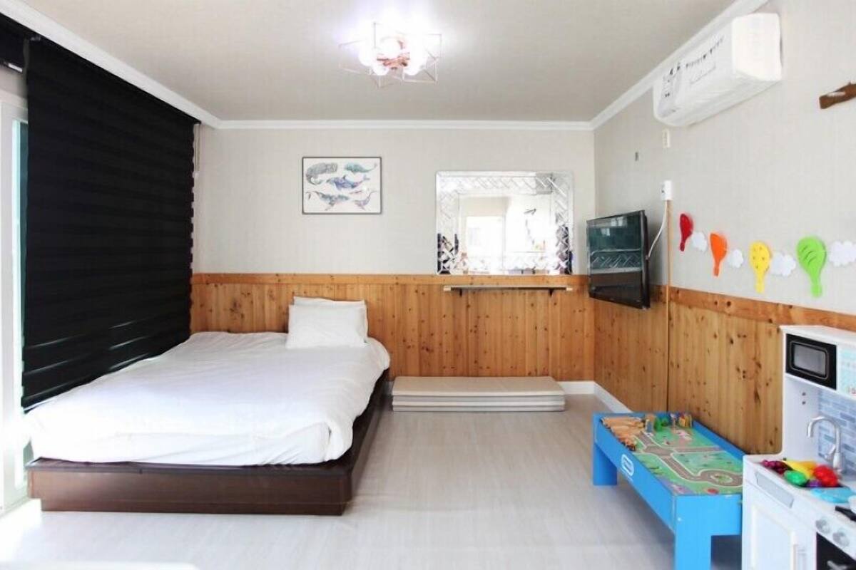A bedroom with a bed, a TV, a children's play area, and a kitchenette.
