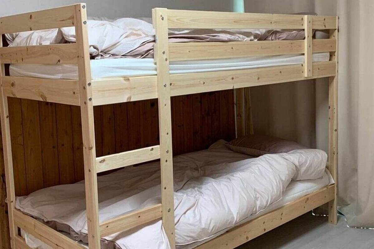 A bunk bed with two levels, wooden frame, and white bedding.