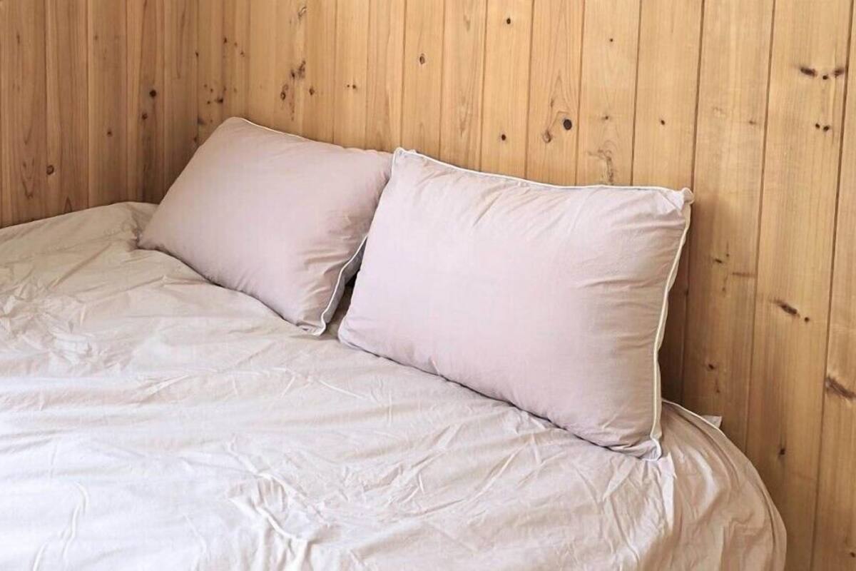 A bed with a white sheet and two pillows against a wooden wall.