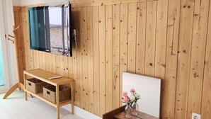 Ein Zimmer mit Holzwandverkleidung, einem an der Wand montierten Fernseher, einer hölzernen Bank mit Körben und einem kleinen Tisch mit Blumen.