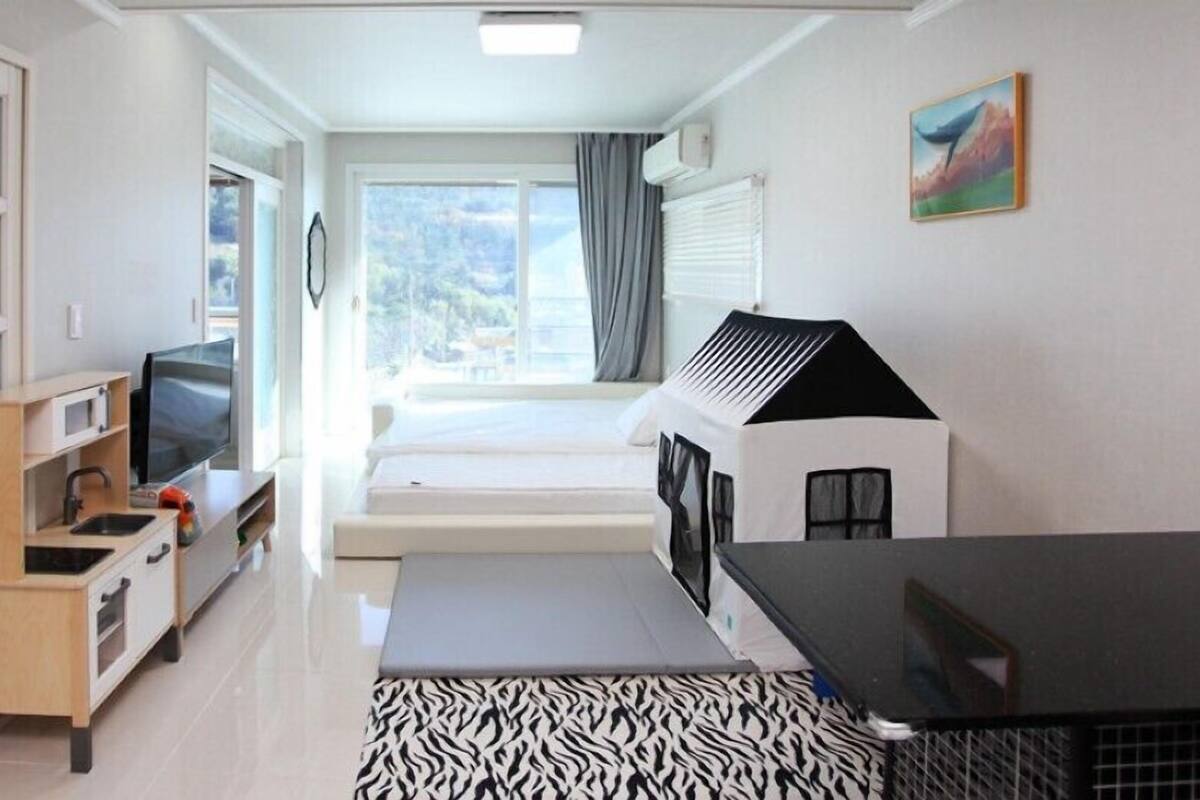 A compact hotel room with a kitchenette, a bed, a playhouse, and a view of the outdoors.