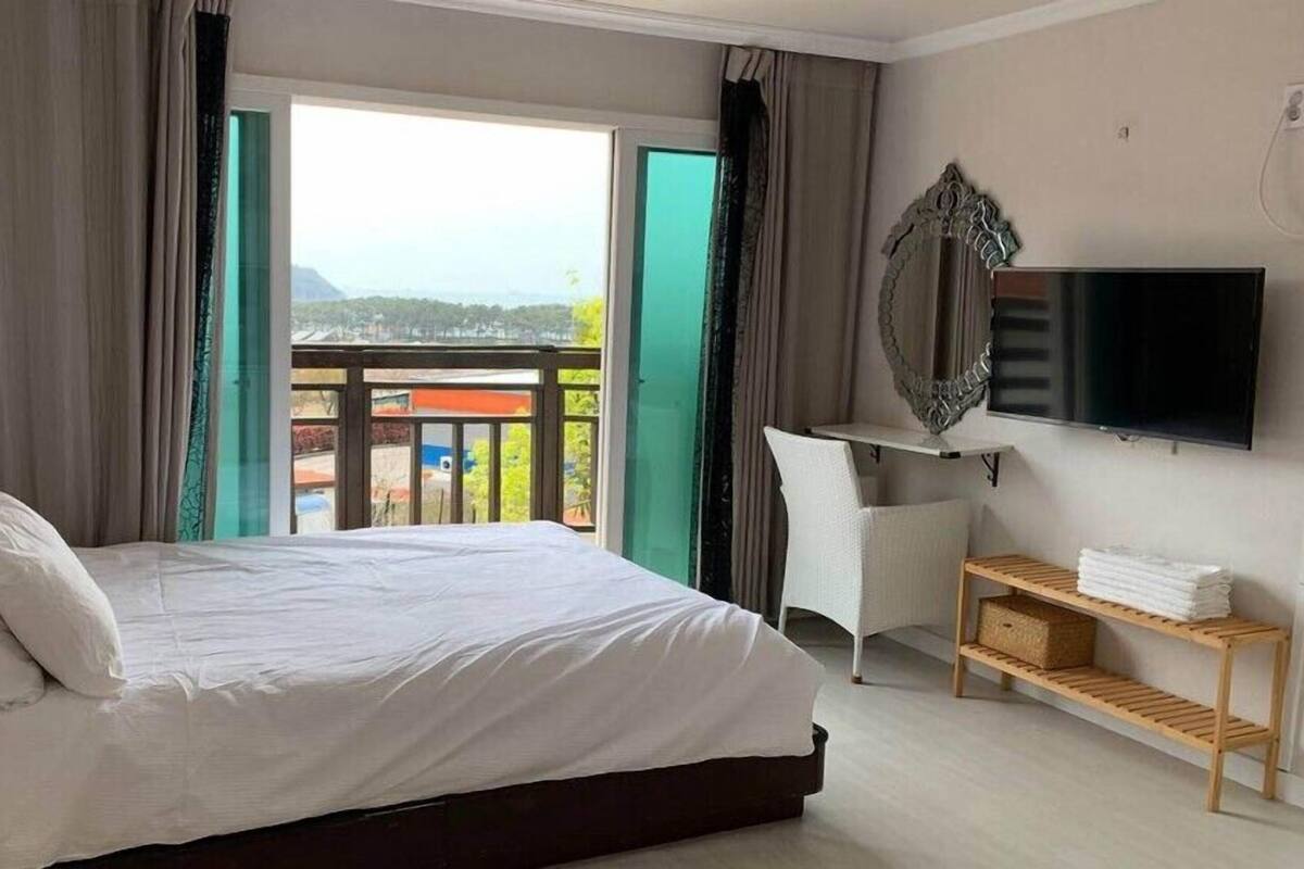 A hotel room with a bed, a desk, a TV, and a balcony with a view.
