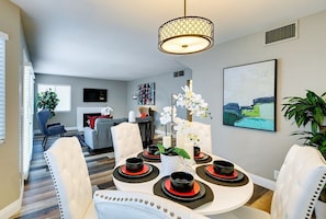 Un coin repas avec une table ronde, des chaises blanches, un lustre et un tableau au mur.