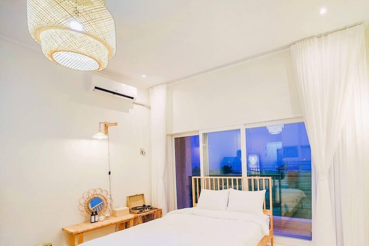 Une chambre moderne avec un grand lit, une table de chevet avec une lampe et une vue sur la ville la nuit.