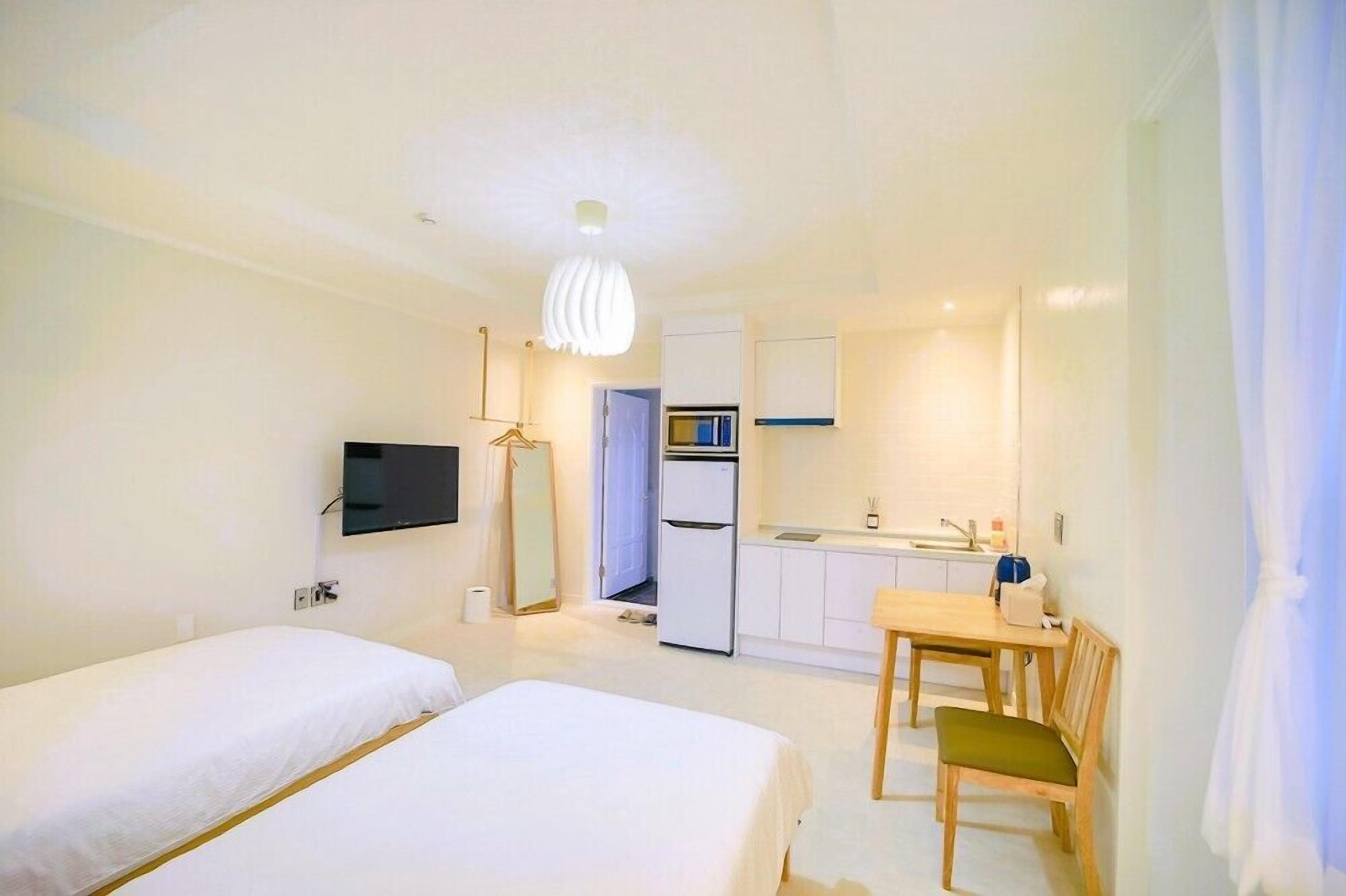 A hotel room with two beds, a TV, a kitchenette, and a dining area.