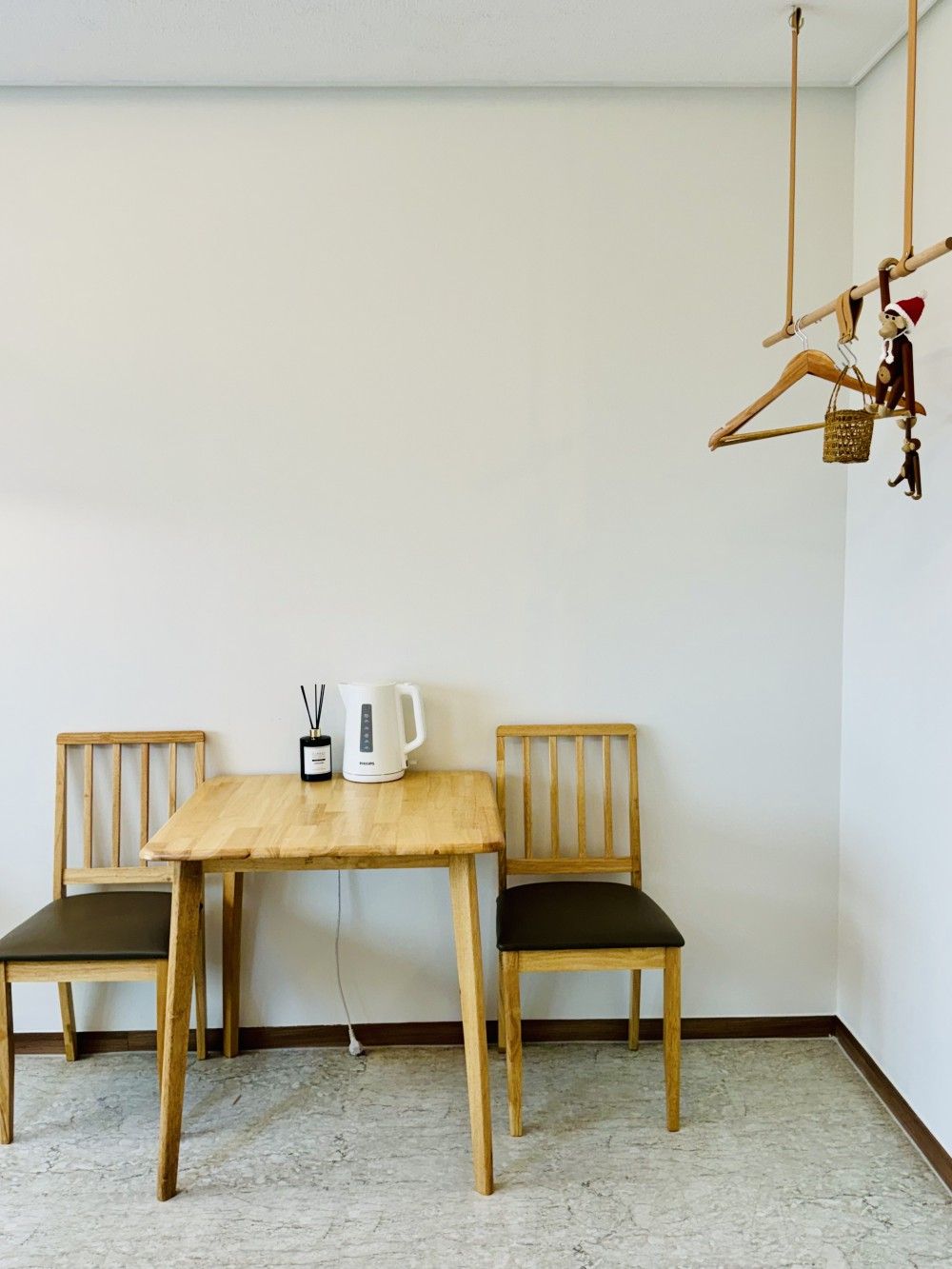 A room with a wooden table and two chairs, a white kettle, and a small decorative item on the wall.
