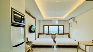 Une chambre d’hôtel avec deux lits, une kitchenette, une télévision et vue sur la mer.