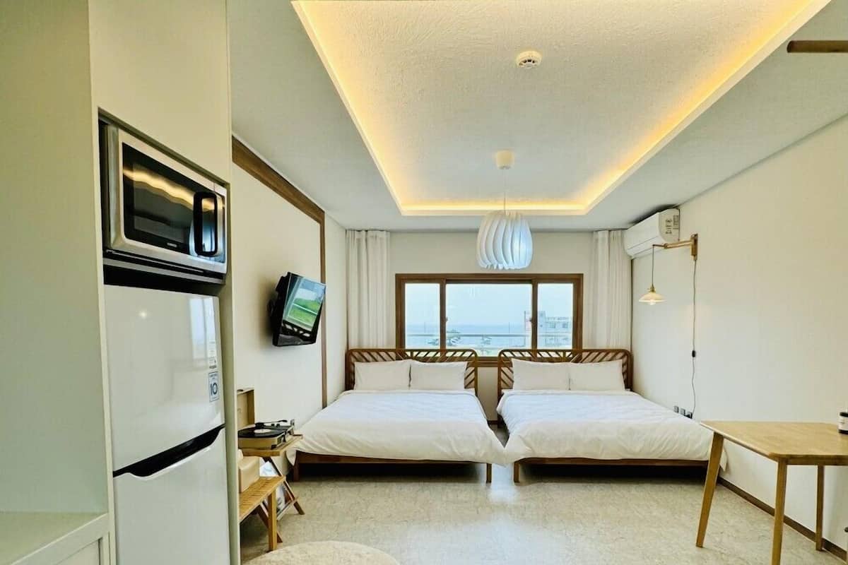 Une chambre d’hôtel avec deux lits, une kitchenette, une télévision et vue sur la mer.